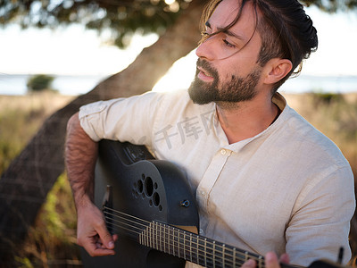 穿着衬衫的吉他手在乡下用灰色吉他唱歌
