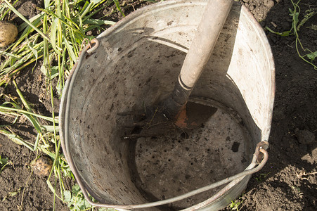 花园土草背景上带耙子的旧脏锈铁桶的特写