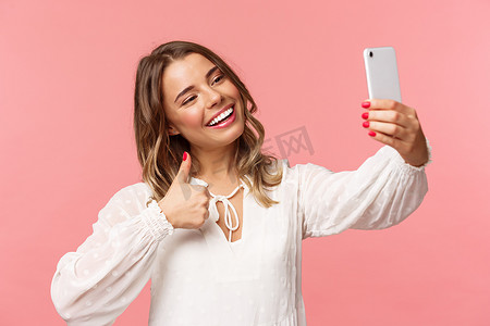 时尚美女博主的特写肖像在智能手机上录制视频，自拍，对着手机摄像头竖起大拇指，高兴地微笑，向追随者推荐地方