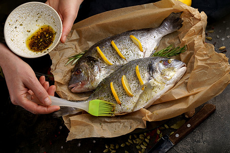 如鱼旗袍摄影照片_新鲜准备烹制生鲷鱼多拉多，配料和调味料，如迷迭香、盐、胡椒、石灰和橄榄油，俯视