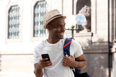 带盖摄影照片_带着手机和包在城市里微笑的非洲裔美国人