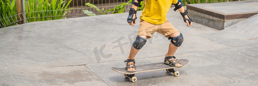 戴着头盔和护膝的运动男孩在滑板公园里学习滑板。
