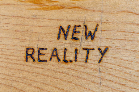 用木材燃烧器工具在平坦的木材表面上手写的“新现实”一词
