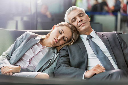 商务夫妇在机场等待登机时睡觉时带镜头光晕的肖像
