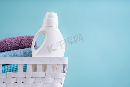 蓝色背景中突显的白色桌子上装有洗涤剂瓶和一堆干净毛巾的洗衣篮