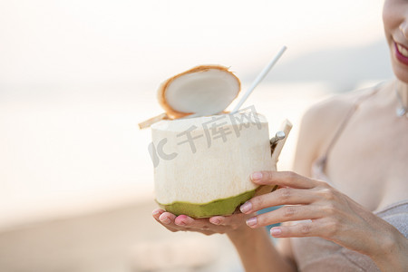 女人在沙滩上喝新鲜椰子，浪漫的日落时刻。