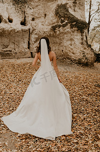 穿着婚纱的新娘在落下的橙叶上穿过秋天的森林跑到山上