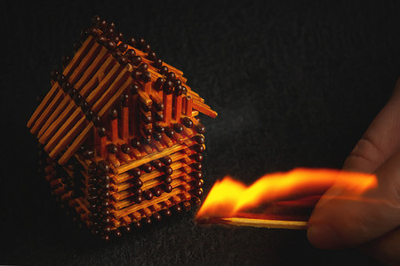 手拿着燃烧的火柴点燃火柴、风险、财产保险保护或可燃材料概念点火的房屋模型