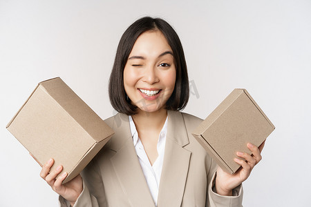 女脸手摄影照片_女售货员的形象，亚洲女商人拿着装有公司品牌产品的盒子，对着镜头微笑，站在白色背景下
