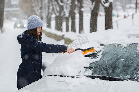 一名妇女正在清除汽车挡风玻璃上的雪。
