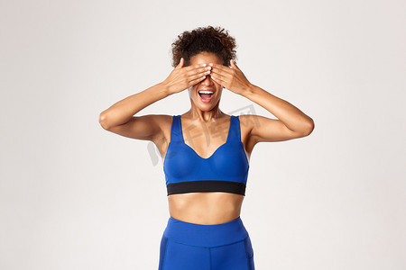 充满希望的非洲裔美国女运动员的工作室照片，身穿蓝色运动服，闭上眼睛，微笑，期待惊喜，白色背景