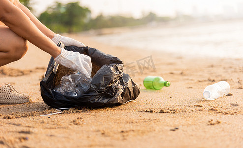为清洁海滩而将塑料瓶捡进黑色垃圾塑料袋的志愿者妇女