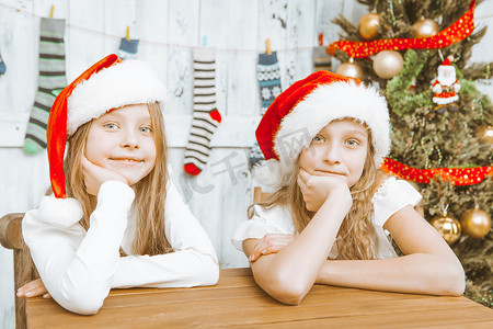 孩子们坐在圣诞树和圣诞奇迹和礼物旁边的桌子旁。