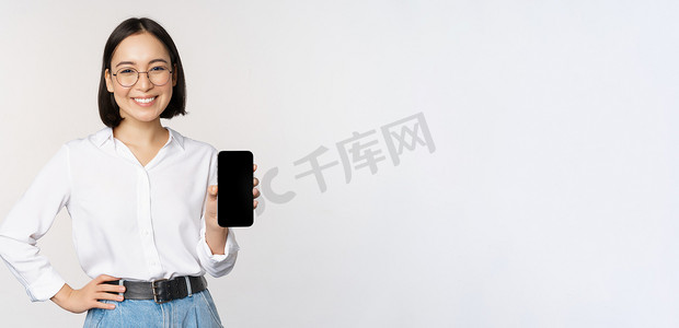 微笑的韩国女性展示智能手机屏幕，展示移动应用程序，站在白色背景上