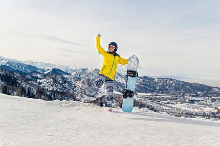 雪山背景中身穿黄色夹克和黑色头盔的年轻女子单板滑雪者