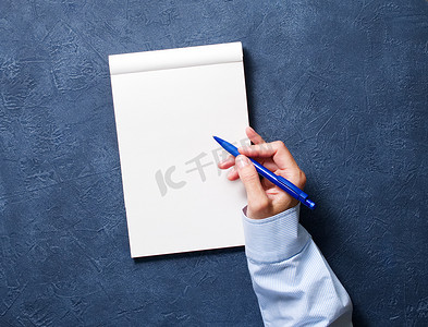 女人在深蓝色桌子上的笔记本上写字，手拿衬衫拿着铅笔，素描本