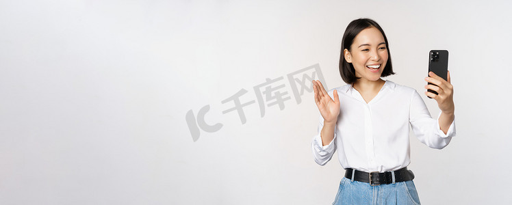 时尚现代亚洲女性对着智能手机前置摄像头挥手、视频聊天、在手机应用程序上与人聊天、白色背景的形象