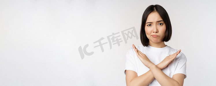 亚洲韩国女性的画像显示停止、禁止手势、显示手臂交叉标志、站在白色背景上的 T 恤