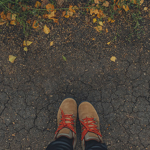 方形图像 棕色靴子脚踩在开裂的地上，上面有黄色的落叶。