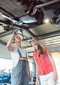 可靠的汽车修理工在现代修理店检查一名妇女的汽车