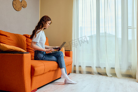橙色客厅摄影照片_漂亮的女人在橙色的沙发上用笔记本电脑聊天
