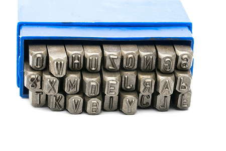 白色背景上隔离的蓝色塑料盒中的一组金属印章字母打孔器