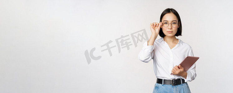 年轻亚洲女商人的形象，戴眼镜的女企业家，拿着平板电脑，戴眼镜看起来很专业，白色背景