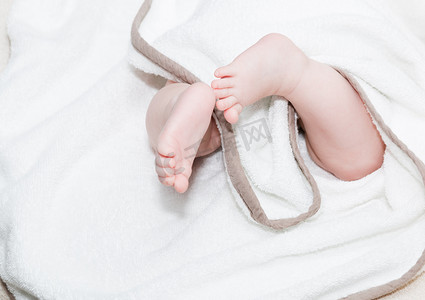 婴儿毛毯摄影照片_婴儿脚在毛巾下。婴儿躺在床上的尿布中，婴儿无法辨认。浅脱。