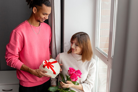 一个时髦的男人给他的女朋友，一个带蝴蝶结的白色心形盒子和一束玫瑰