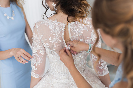 女手为留着漂亮发型的新娘扣上婚纱。