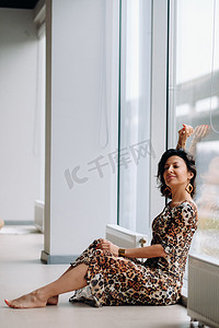 一个穿着虎裙的黑发女人坐在室内的一扇大窗户前