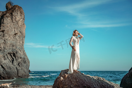 沙滩装饰摄影照片_中年妇女金发碧眼，波西米亚风格，脖子和手臂上戴着白色长裙，戴着沙滩装饰。