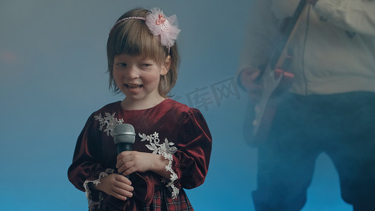 穿着复古裙子的小女孩在舞台上唱歌，她的父亲弹着电吉他