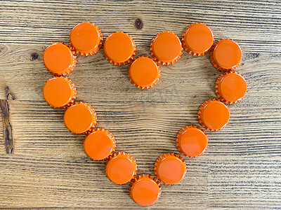 橙色爱心摄影照片_一颗由啤酒瓶制成的橙色爱心，盖在质朴的盖子上