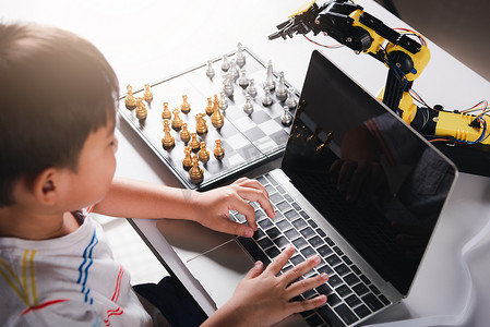 孩子的未来未来摄影照片_亚洲小男孩编程代码到笔记本电脑上的机器人机械臂下棋