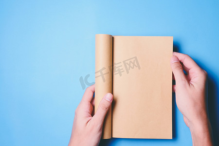 拿着本摄影照片_手拿着一本空白书的顶视图，准备好复制空间，准备好蓝色背景上的文本。