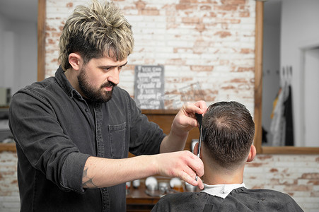 理发师用剪刀给一个英俊的小伙子剪头发。
