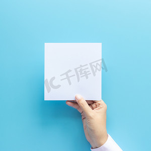手拿车票摄影照片_女人手拿着空白纸页隔离在蓝色背景与复制空间。