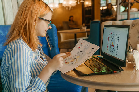 2021 年 8 月 2 日，俄罗斯特维尔。一家咖啡馆里，一位女士拿着笔记本电脑坐在桌边，正在研究一个人的设计。