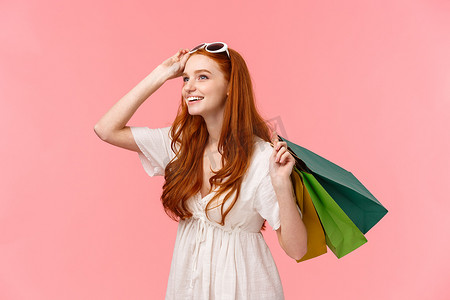 有趣而好奇的年轻红发女孩在商店里购买有趣的商品，看起来很感兴趣，微笑着穿过商场，把袋子放在袋子后面，摘下眼镜