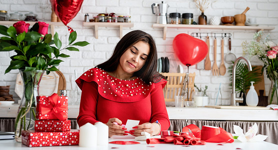 气球情书摄影照片_穿着红色裙子的年轻浪漫女人坐在装饰精美的厨房里写情书