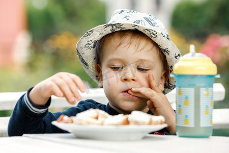 在夏日花园的背景下，男孩早餐时吃烤面包和果汁