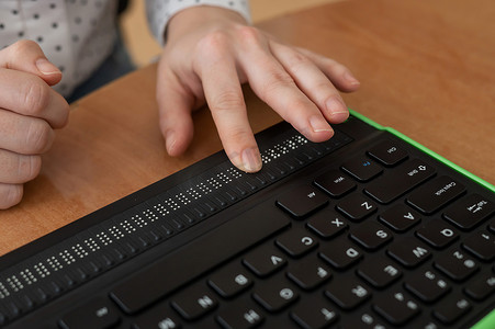 一位盲人妇女使用带有盲文显示器和电脑键盘的电脑。