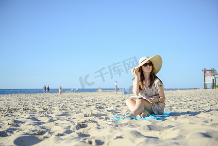 书的海洋摄影照片_一个年轻的黑发女人在海滩上放松、阅读博文的肖像