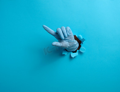 一只戴着蓝色医用手套的手从蓝纸背景的破洞中伸出，食指举起。