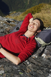 微笑的年轻女子躺在巨石上，头枕在背包上