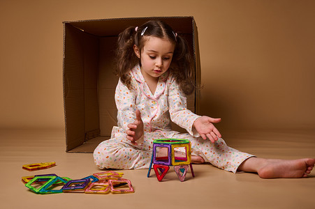 集中美丽的欧洲学龄前女孩玩很多彩色塑料块建造者和建筑房子。