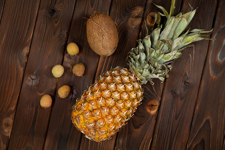 荔枝品种摄影照片_异国情调的水果：棕色木质背景中的菠萝、椰子和荔枝