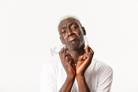 好运满满摄影照片_可怜的非洲裔金发男子的特写镜头，恳求或乞求，许愿，交叉手指祝你好运，用绝望的表情祈祷，白色背景