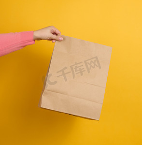 女人手里拿着棕色空白牛皮纸袋，用于黄色背景的外卖。